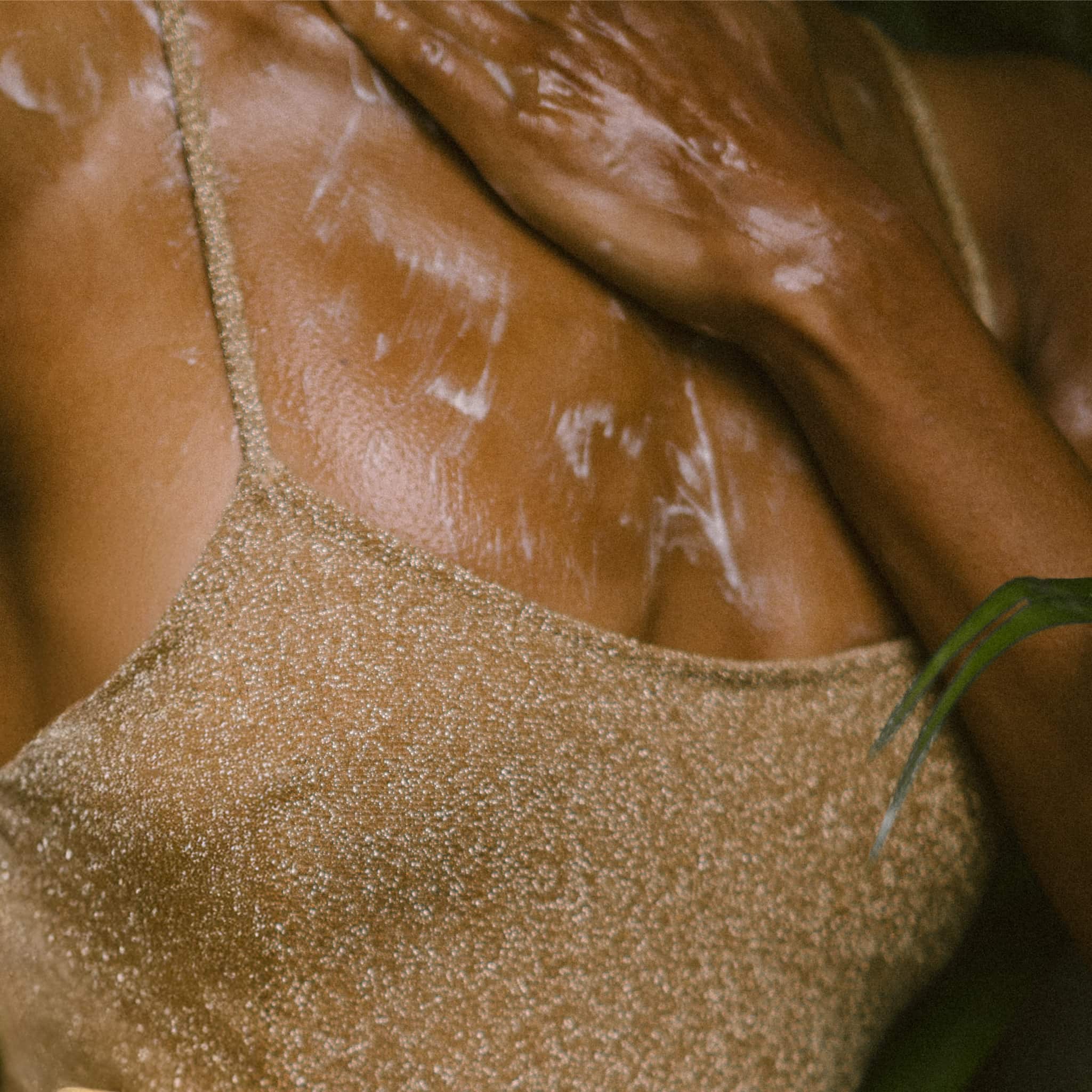 Close-up of a model wearing a gold glitter swimsuit top and applying ECO BY SONYA Body Wash.