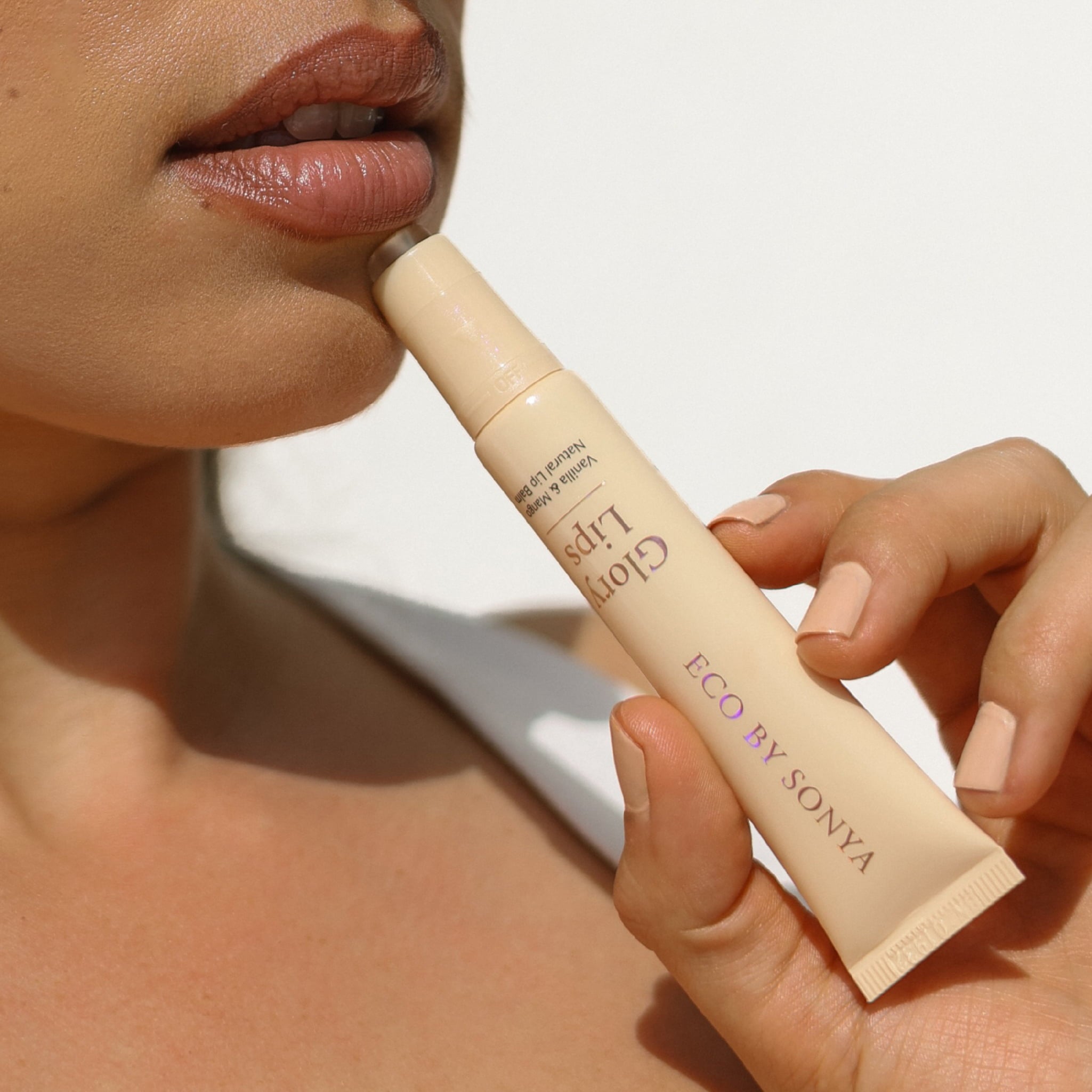 Flat lay of an Eco By Sonya Glory Lips lip balm tube and a mirror styled on a dark brown marble surface.