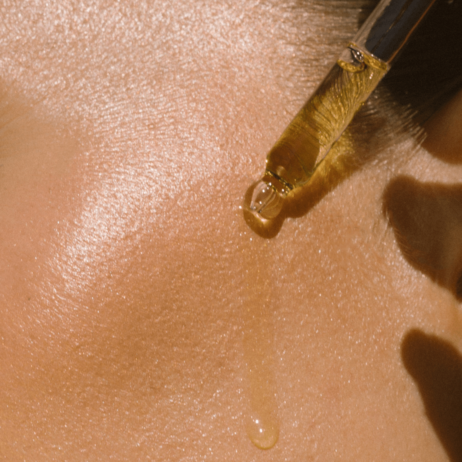 Close-up of dropper releasing a drop of Eco By Sonya Glory Oil onto smooth hydrated skin, showing rich golden oily texture and glow.