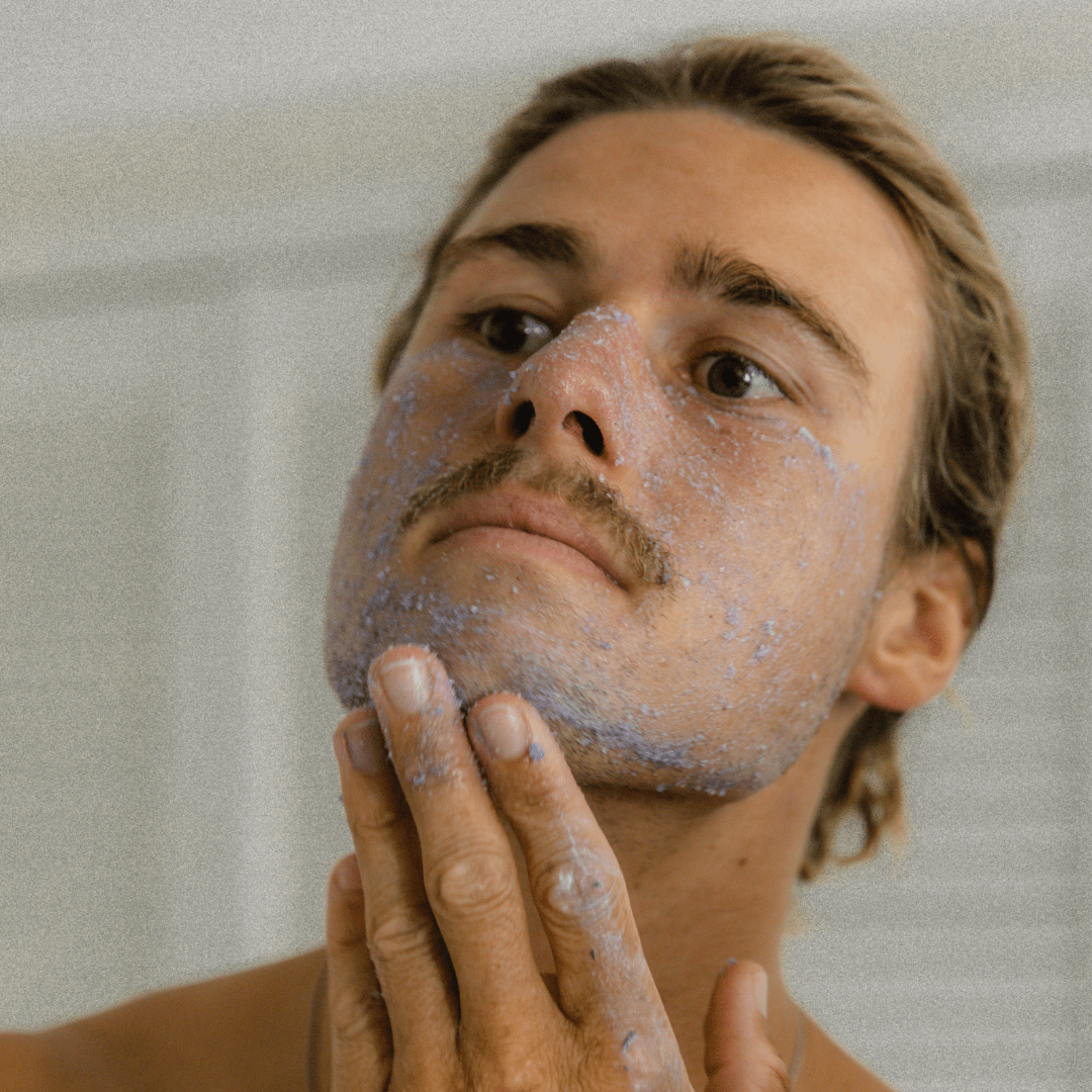 Man applying purple Super Acai Exfoliator with a neutral background