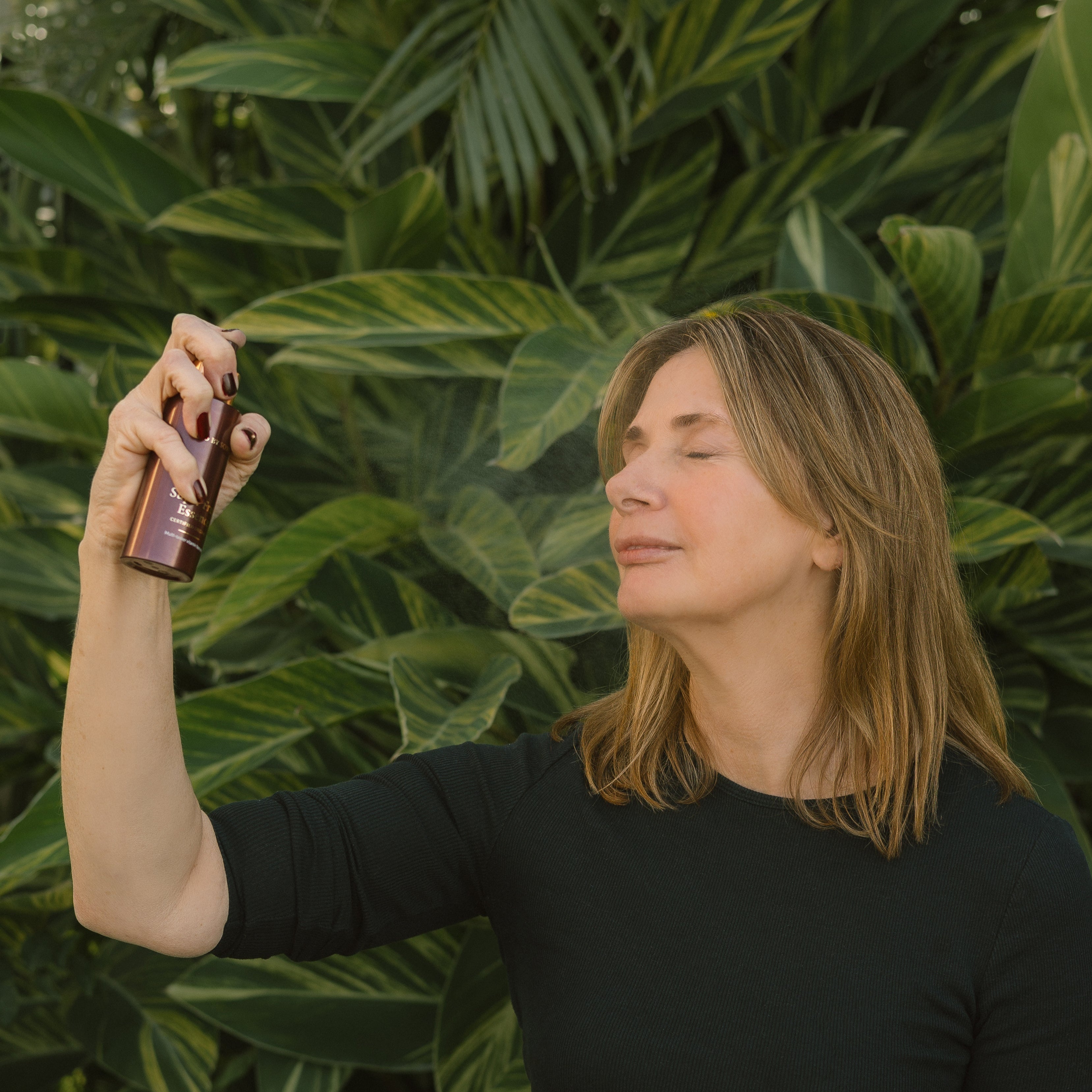 Woman holding a bottle of hair product against a green leafy background